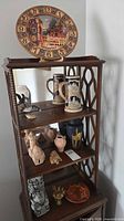 Full shelving unit with all items visible including clock plate, beer steins, statue, brass holder and misc ceramics