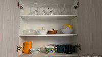 Cabinet view showing wine glasses, casseroles, bowls and mugs