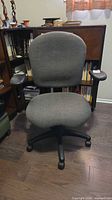 Front view of grey fabric office chair with armrests and wheeled base