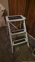 Full view of front of white folding three-step stool with black treads