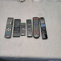 Front view of six remote controls showing brand logos and button layouts