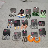 All 15 pairs of Paparazzi earrings arranged on grey surface showing variety