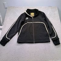 Front view of black US Ski Team jacket showing piping, logo, pockets, cuffs, zipper