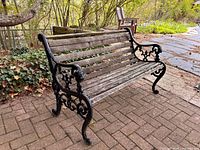 Full view of bench on brick patio showing ornate cast metal sides and weathered wood slats