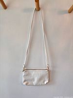 Full view of white faux-croc crossbody bag hanging, showing overall shape and strap length