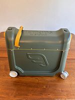 Front/side view of olive JetKids BedBox showing wheels and mustard lid strap
