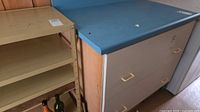 Front and side view showing drawers, handles, blue laminate top, adjacent shelving not included