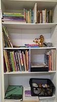 Full bookshelf with assorted books, plush dog, plastic rhinoceros, decorative items in crate