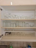 Cabinet shelf showing varied clear glass stemware, tumblers, beer mug, small bowl