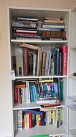 Four-shelf bookcase filled with hardcover and paperback books of assorted subjects