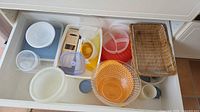 Drawer view showing majority of plastic containers, bowls, juicer and lids
