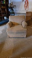 Front view of beige upholstered armchair showing rolled arms, skirted base, overall wear