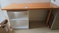 Full view of desk showing light brown top, white shelving unit, right wooden support