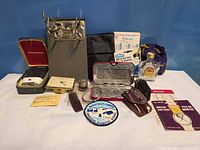 Group shot of all items including shaver, film clip, battery card, clock, eyeglasses case, brush, patch, whisky bottle and bag