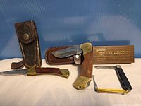 Group view of four folding knives, two leather sheaths, wooden Schrade block