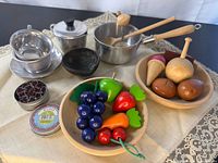 Full lot overview showing wooden play food, stainless cookware, black mortar, tin with cutters