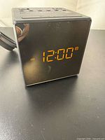 Front view showing LED display reading 12:00 and attached power cord