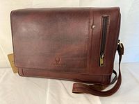 Front view of brown leather messenger bag showing flap, vertical zip pocket, shoulder strap and tag