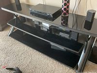 Front view of black glass TV stand showing three shelves and metal legs