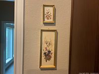 Both framed pressed flower pieces on wall for scale