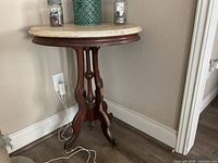 Full view of wood pedestal table with marble top against wall