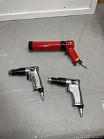 Group shot: two silver air drills and red pneumatic caulking gun