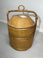 Front view of cylindrical woven basket showing lid and wood handle