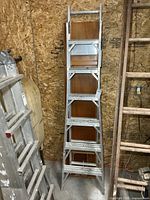 Full view of folded aluminum combination ladder leaning against wall