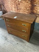 Front view of wooden dresser showing three drawers and brass-tone handles