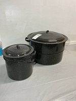 large and small enamel pots side by side with lids on