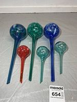 Six glass watering globes arranged upright showing size and color variation