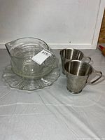 lot overview showing glass measuring pitcher on glass plate beside two stainless measures