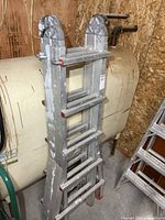 Full view folded four-section aluminum ladder leaning against tank
