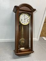 Front view of wooden wall clock showing dial and pendulum