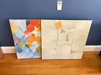 Front view showing both square canvases leaning against wall