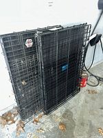 Two folded black wire dog crates leaning against wall