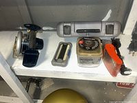 Shelf view showing Ryobi saw, grey case, Dremel case, Porter-Cable wheel, Deckmate screws, red stapler