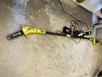 Full view of Ryobi pole saw with batteries and charger on floor
