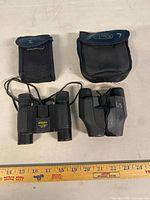 Both binoculars front view with cases and ruler for scale