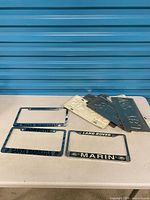 Overview of three license plate frames and stack of novelty plates on table