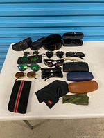 Overall lot view showing all sunglasses, cases, and cloths on table