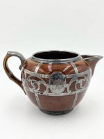 Right side view of brown treacle-glaze creamer with sterling silver overlay detailing