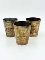 Three engraved brass cups standing