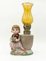 Front view of figurine lamp showing girl, basket base, brass burner, amber chimney