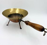 Angled view showing copper exterior, brass interior, three legs, and wooden handle