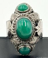 Front view of sterling silver poison ring showing three green onyx cabochons and floral repoussé design