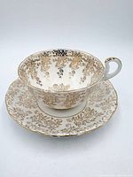 Royal Vale teacup on matching saucer showing gold floral pattern, white background, gilt trim