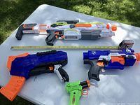 All four Nerf blasters and two magazines on table with tape measure