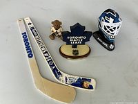 Lot overview showing both mini sticks, teddy bear, desk plaque, and goalie mask