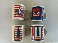 Front view of all four mugs showing different patriotic Coca-Cola designs